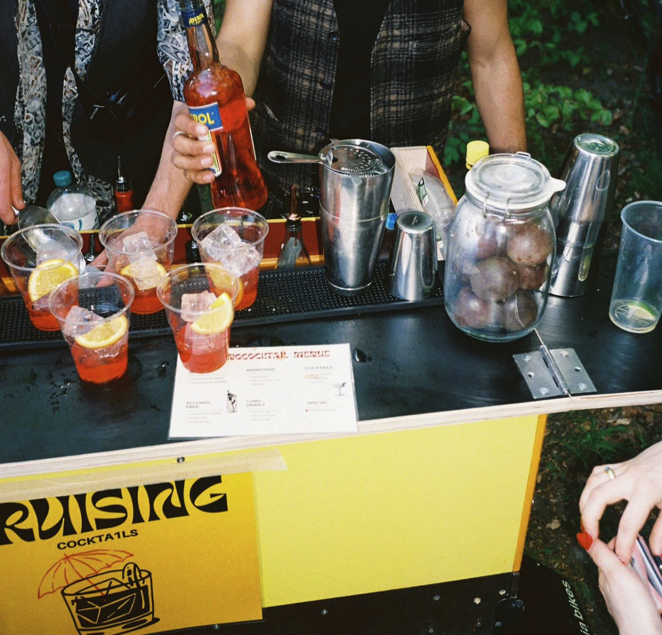 Reihe frisch gemixter Aperol-Drinks mit Orangenscheiben auf der Bar-Theke des gelben Carts
